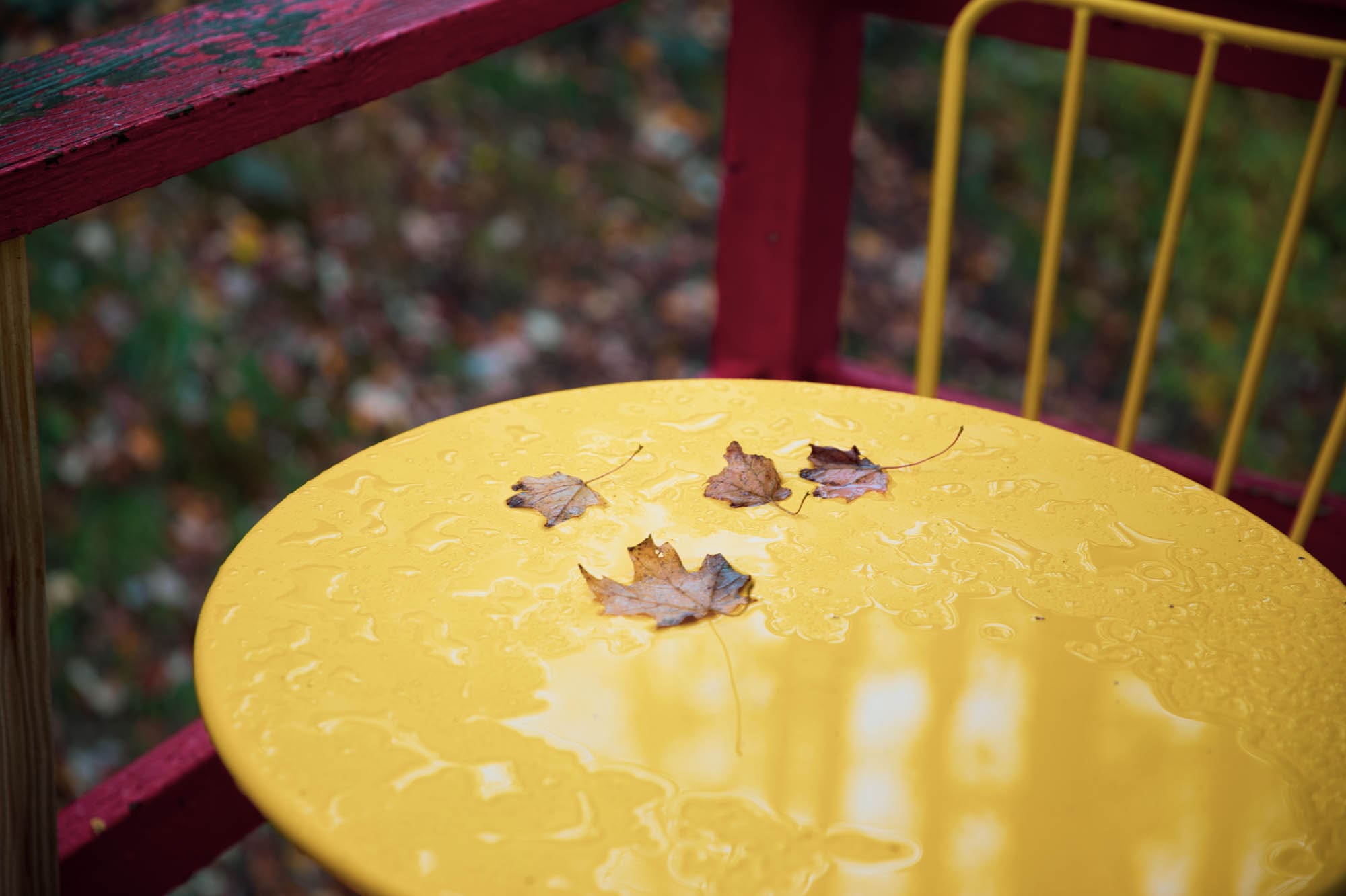 Yellow bistro table on the front deck dusted with autumn leaves